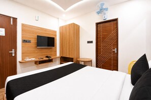 Habitación de hotel con cama, televisor montado en la pared, armario de madera, una mesita y una puerta con detalles decorativos.
