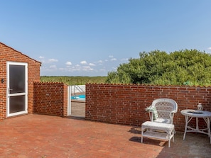 Eine Terrasse mit Backsteinmauer, einem weißen Stuhl, einem kleinen Tisch und einem Pool im Hintergrund.