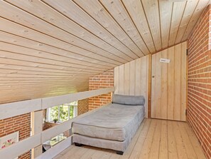 Una habitación pequeña y cerrada con una cama individual, techo de madera y paredes de ladrillo.