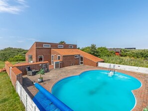Ett tvåvåningshus med en swimmingpool, en uteplats och en byggnad med rött tak i bakgrunden.