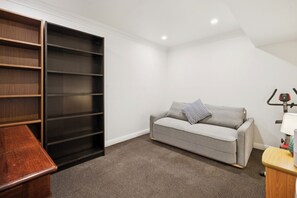 A room with a grey sofa, a black shelving unit, and a small wooden table. - Riezel House with Outdoor Spa and Sauna (Leura)