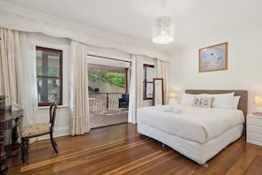 A bedroom with a large bed, a desk, and a chair. There is a balcony with a view of greenery. - Riezel House with Outdoor Spa and Sauna (Leura)