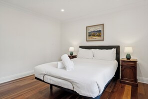 A neatly made bed with white linens and two pillows, a bedside table with a lamp, and a painting on the wall. - Riezel House with Outdoor Spa and Sauna (Leura)