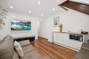 A modern living room with a sofa, a flat-screen TV, a small kitchen area with a microwave, and a wooden floor. - Riezel House with Outdoor Spa and Sauna (Leura)