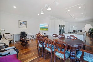 A spacious dining area with a large wooden table and chairs, a kitchen in the background, and artwork on the walls. - Riezel House with Outdoor Spa and Sauna (Leura)