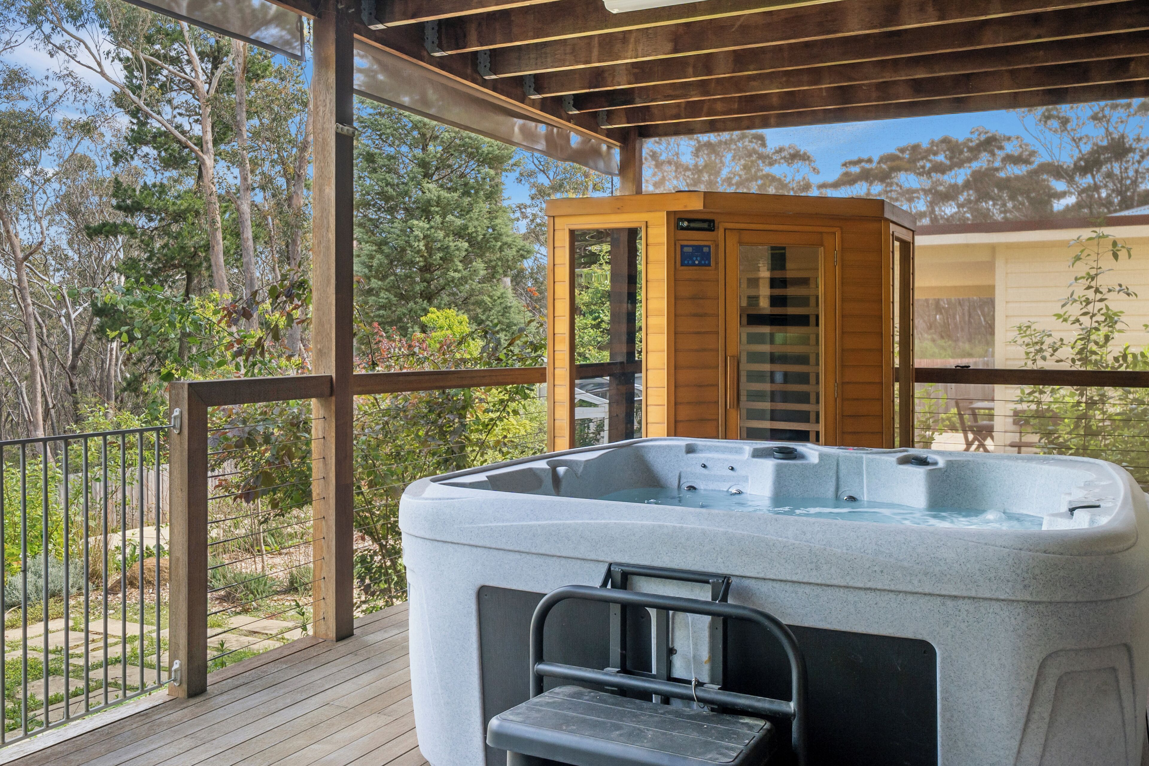 Ein Whirlpool auf einer Holzterrasse, im Hintergrund eine Saunalodge aus Holz.