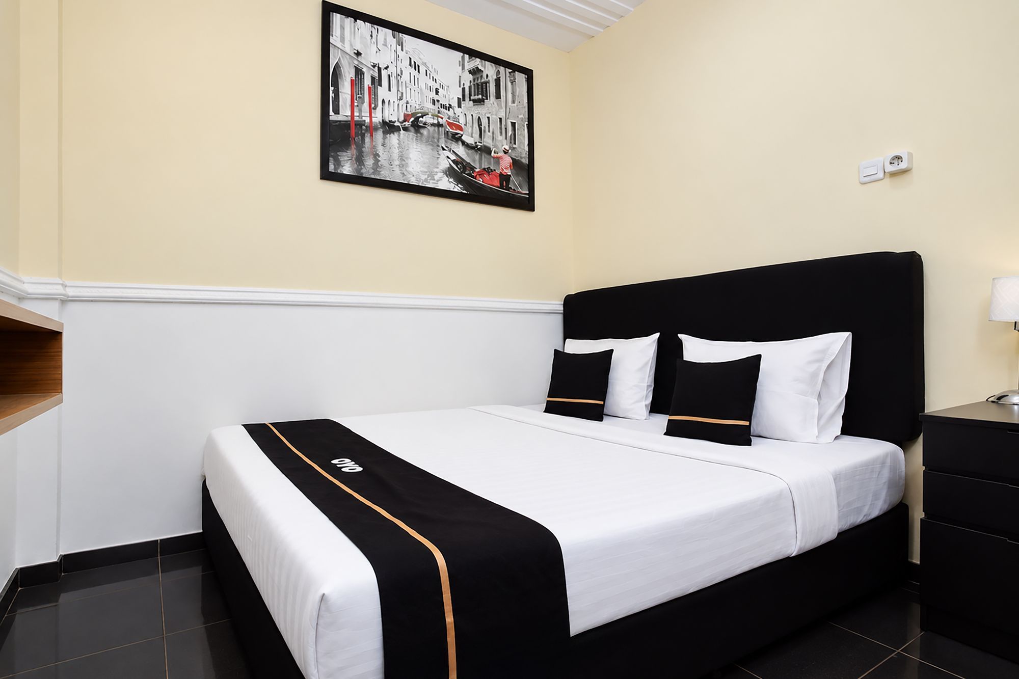 A hotel room with a bed, a nightstand, a lamp, and a painting on the wall.