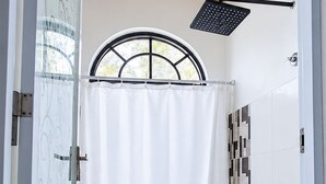 Un baño con inodoro, ducha y ventana con cortina.