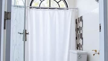 Un baño con inodoro, ducha y ventana con cortina.
