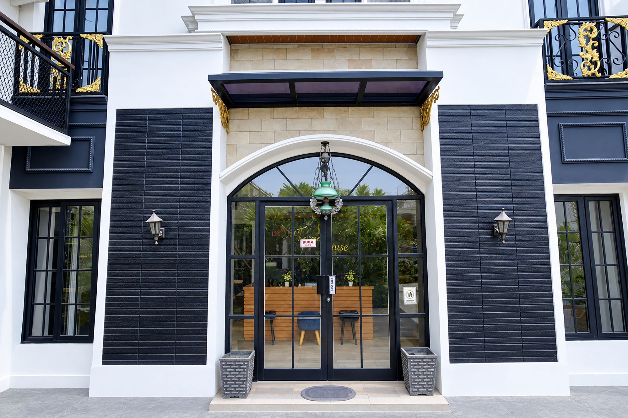 A building entrance with a black and white facade, a glass door, and a small outdoor seating area visible through the door.