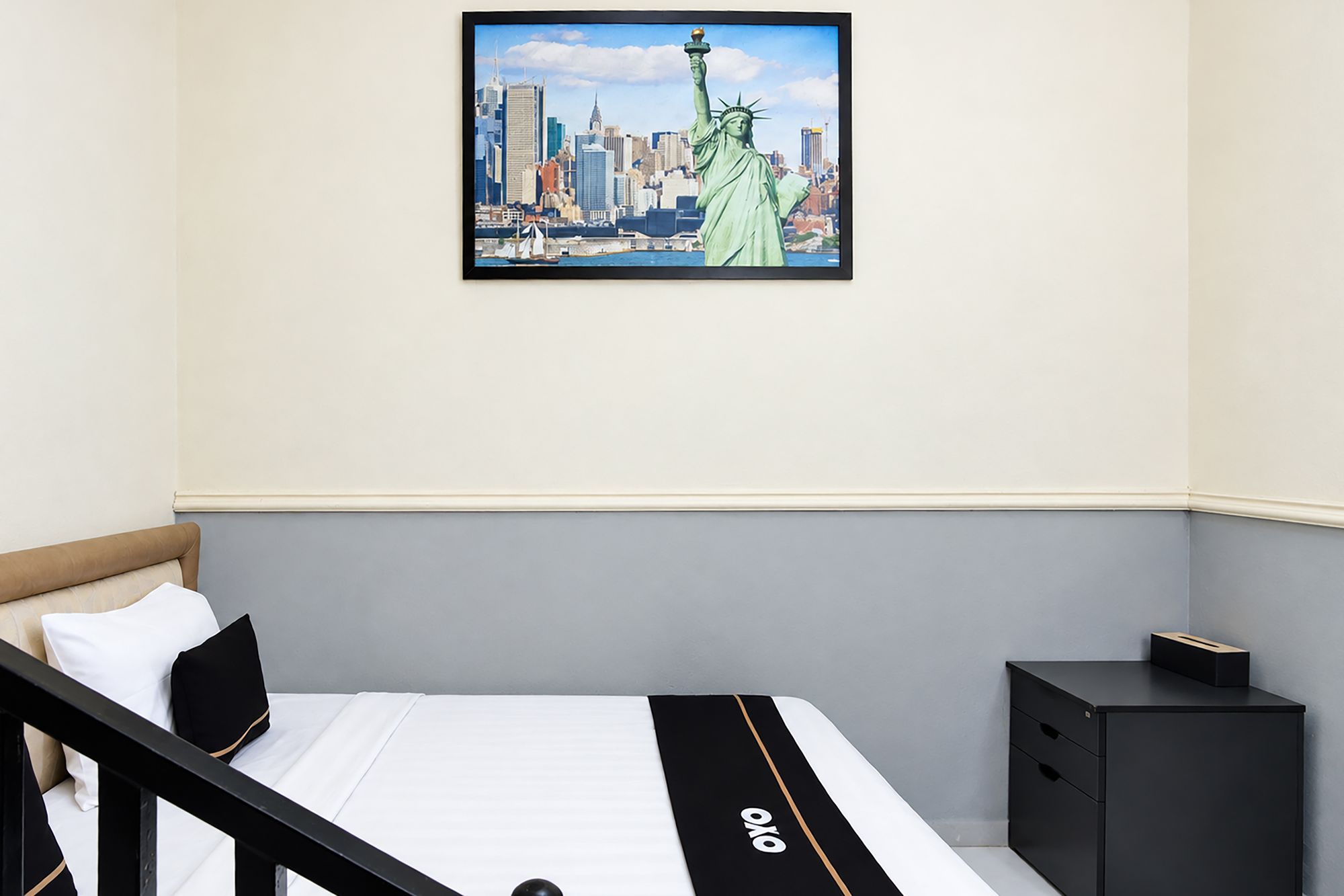 Habitación de hotel con cama, mesita de noche, un cuadro enmarcado de la Estatua de la Libertad y un horizonte urbano.