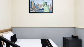Habitación de hotel con cama, mesita de noche, un cuadro enmarcado de la Estatua de la Libertad y un horizonte urbano.