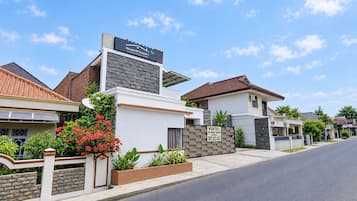 A residential street with modern houses, a clear sky, and a sign for 'House Of Tuwuh'.