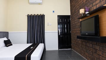 A hotel room with a bed, a black door, a mounted TV, and a wall-mounted air conditioner.