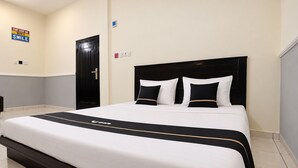 Una cama bien hecha con cabecera y colcha blanco y negro, y un cartel en la pared que dice 'EMPIEZA CADA DÍA CON UNA SONRISA'.