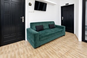 A green sofa in a room with wooden flooring, a black door, and a TV mounted on the wall. - Hotel O near Mall Boemi Kedaton 1 (Bandar Lampung)