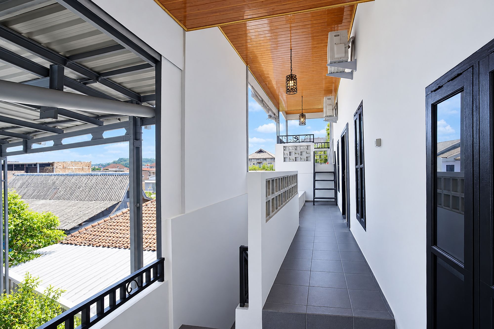 A corridor with a view of the outside, a wooden ceiling, and a black door on the right.