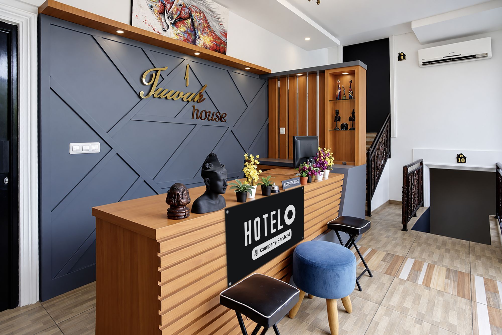 A hotel reception desk with a modern design, a reception area, and a staircase leading to an upper floor.