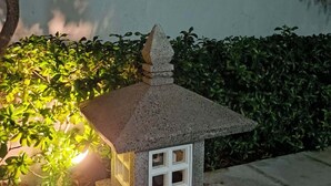 En liten, upplyst modell av ett traditionellt japanskt hus med ett tak täckt av tegelpannor, placerad på en sockel av sten.