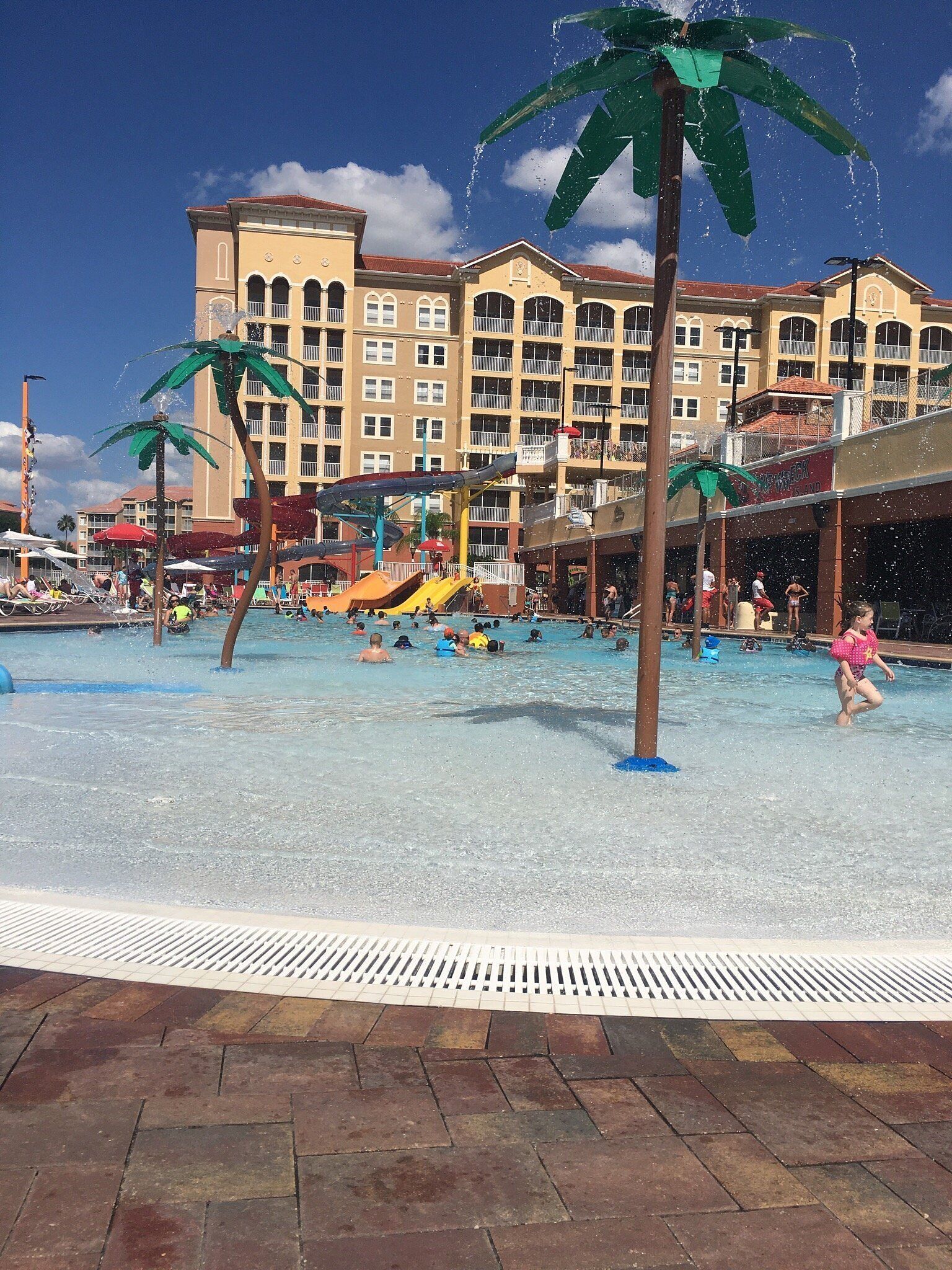 Ein Wasserpark mit mehreren Rutschen und Pools, umgeben von einem Hotel mit Balkonen und blauem Himmel.