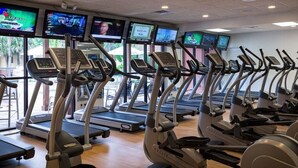 Ein Fitnessraum mit mehreren Laufbändern und Ergometer, ausgestattet mit digitalen Bildschirmen, die unterschiedliche Inhalte zeigen.