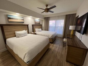 Habitación de hotel con dos camas, un escritorio, una silla, un ventilador de techo y una ventana con cortinas.