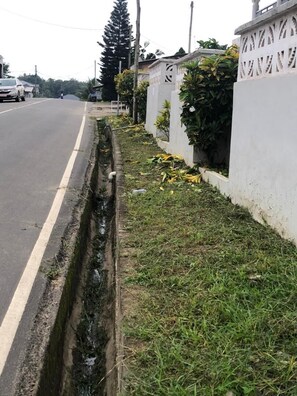 A road with a drainage ditch alongside a white wall with decorative patterns. - Sunset View Guest House (Sekondi-Takoradi)