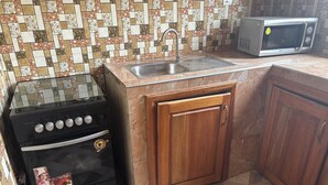 A kitchen with a stove, sink, microwave, and wooden cabinets. - Sunset View Guest House (Sekondi-Takoradi)