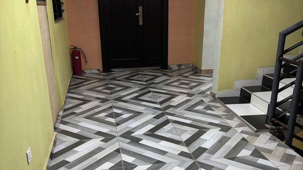 A hallway with a geometric patterned floor, a black door, and a staircase with a metal railing. - Sunset View Guest House (Sekondi-Takoradi)