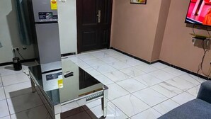 A room with a glass-top table, a sofa, a television, and a refrigerator. - Sunset View Guest House (Sekondi-Takoradi)