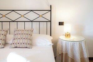 Uma cama bem arrumada com almofadas estampadas, uma mesa de cabeceira com abajur e um quadro pendurado na parede.