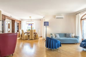 Ampla sala de estar com mesa de jantar, cadeiras, sofá e abajur.