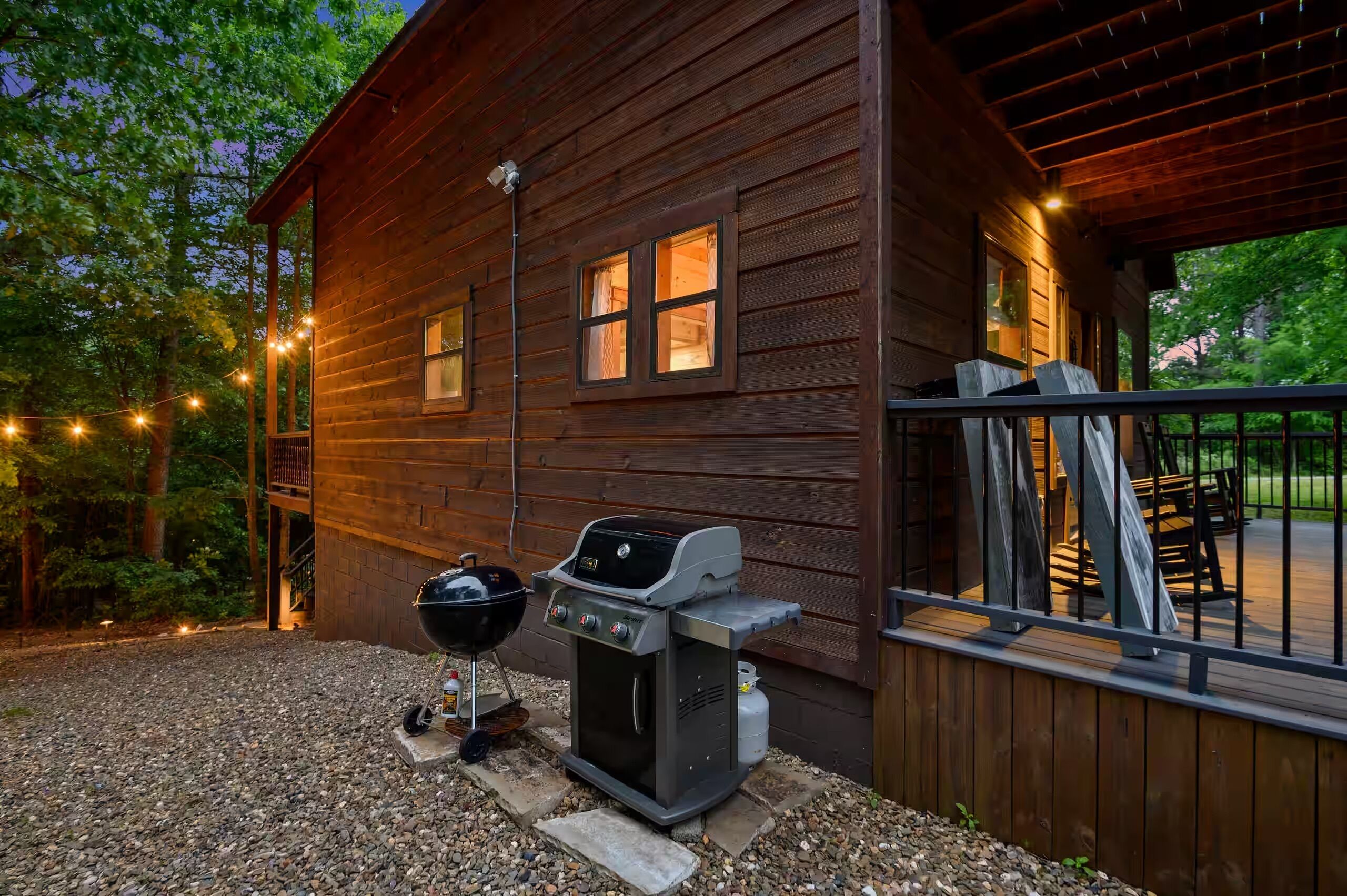 Una cabaña de madera con una parrilla al aire libre, un porche cubierto y luces colgantes.