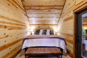 A wooden cabin room with a bed, bench, and two lamps.