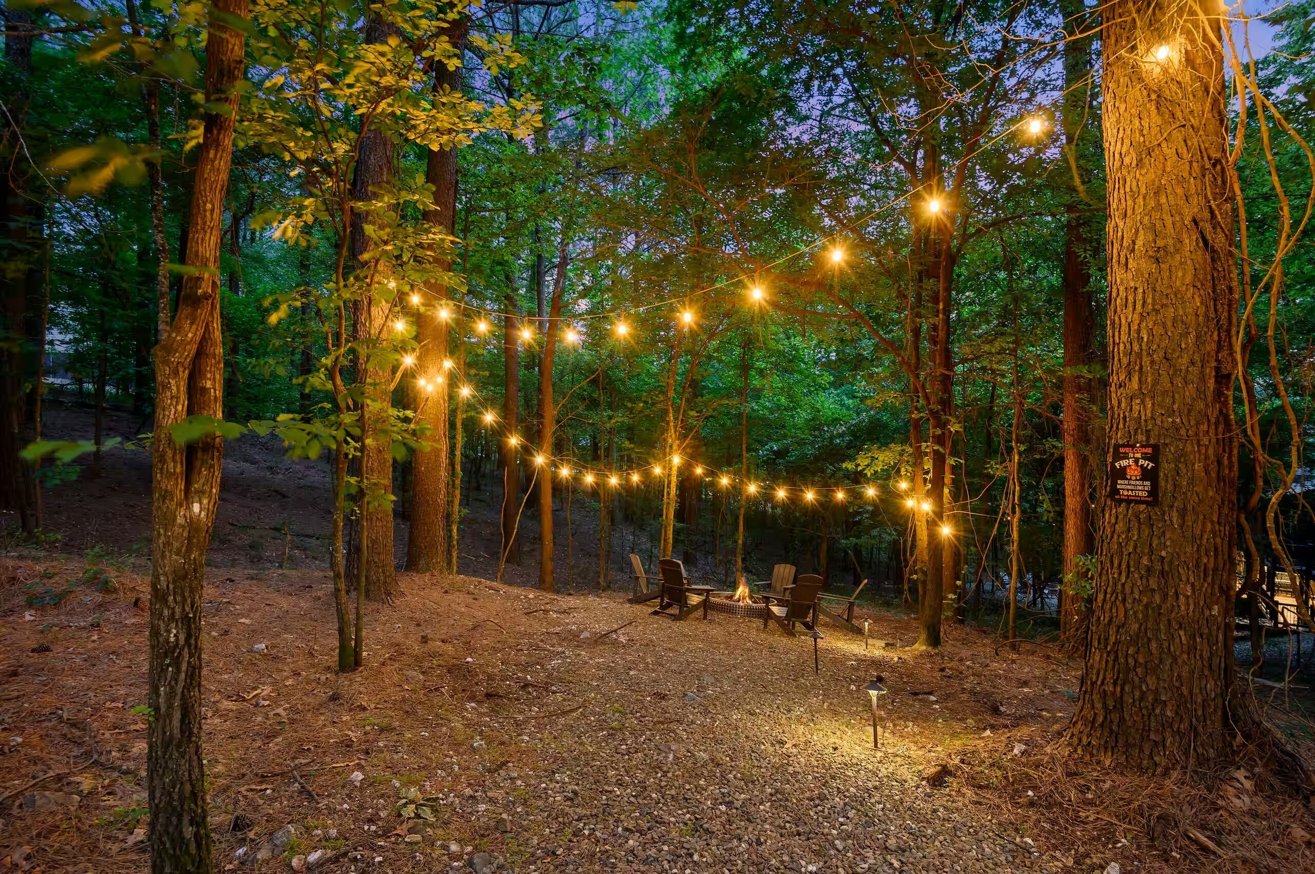 Un camping con luces de cuerda, un hogar y un letrero de bienvenida en un área boscosa.