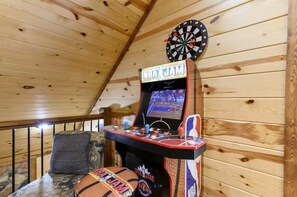 Darts-taulu, koripallopeli ja pehmustettu penkki puisessa huoneessa.