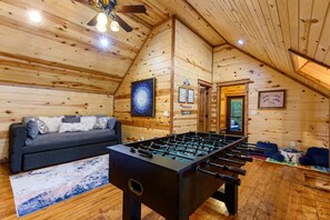 A cozy room with a foosball table, a sofa, and wooden walls.
