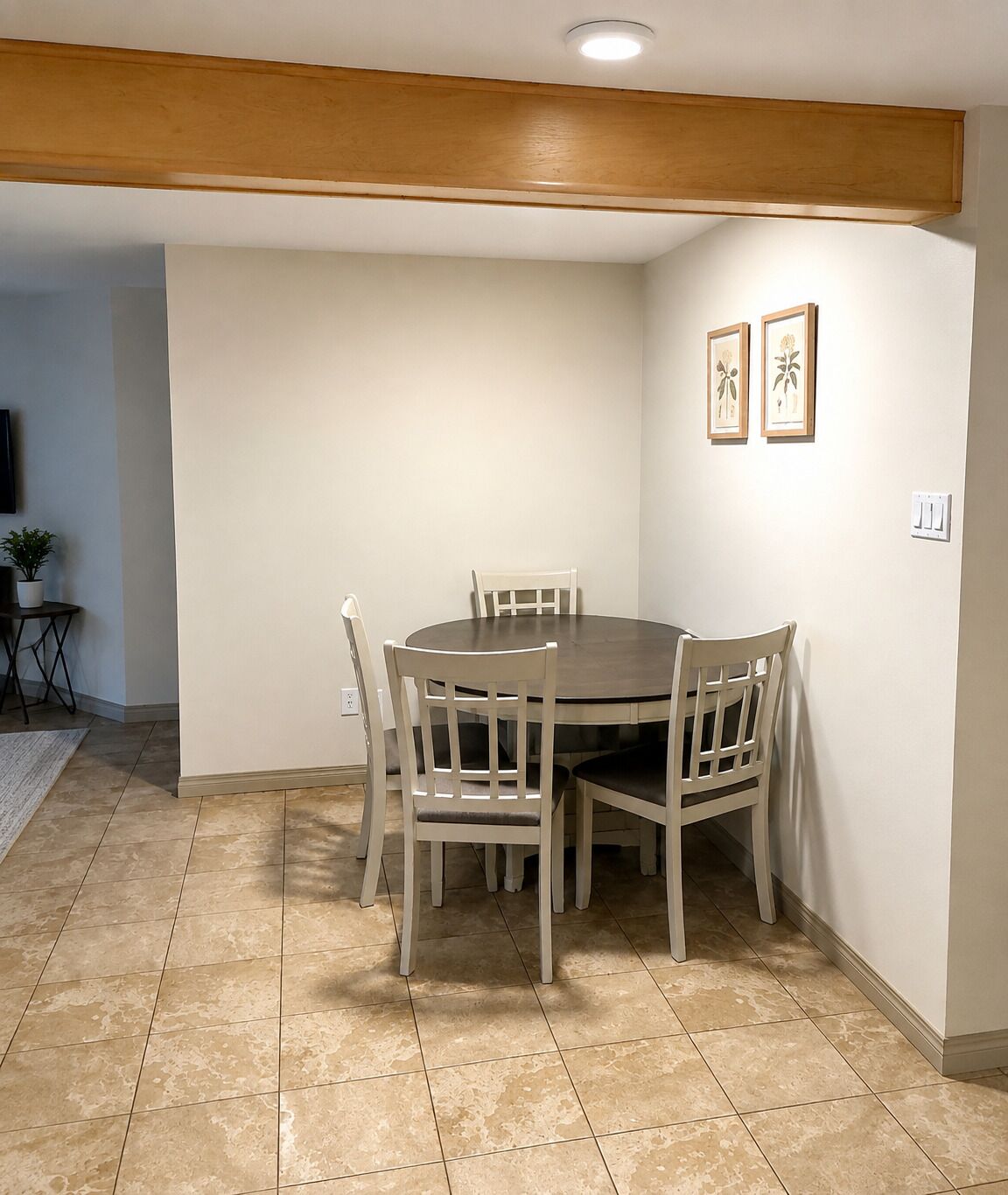 A dining area with a round table and six chairs, a wooden ceiling beam, and a tiled floor.