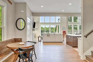 A spacious living area with a dining table, chairs, and a sofa. There is a kitchen area with a countertop and a staircase leading to another level. - The Gathering Place (Mineral)