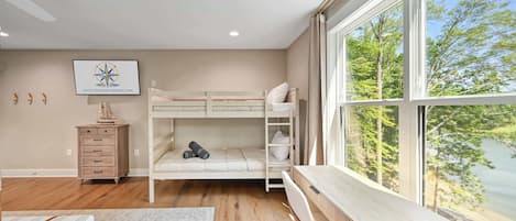 Un dormitorio con una cama nido, un escritorio de madera, un aparador y un ventanal con vistas a árboles.