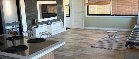 A modern kitchen with a central island, a dining area with a sofa, and a large window with blinds.