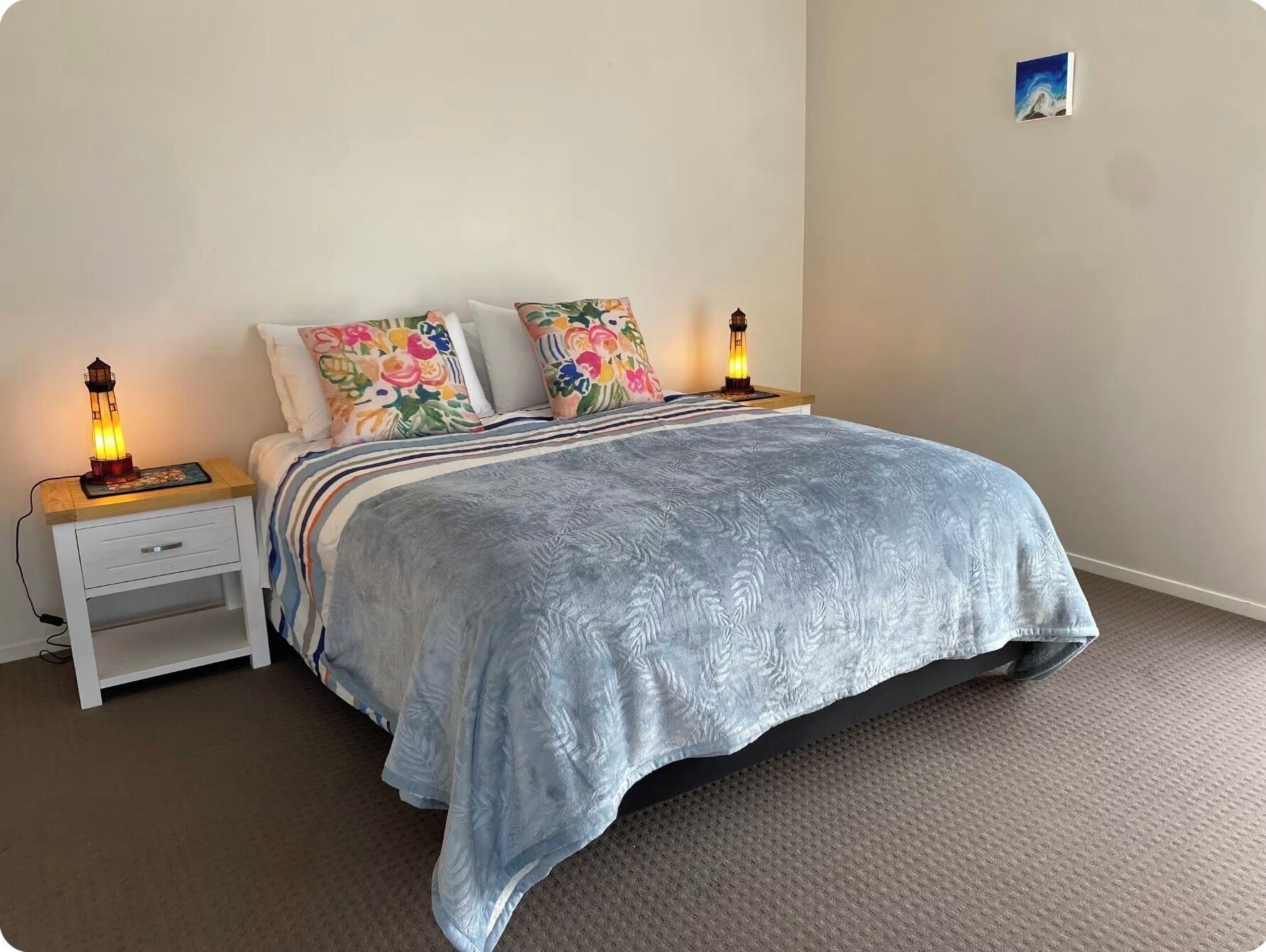 A bedroom with a bed, two bedside lamps, a nightstand with a drawer, and a wall-mounted picture.