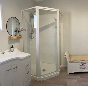 Une salle de bain moderne avec une douche à parois de verre, un meuble-lavabo blanc doté de tiroirs, un miroir rond et une petite étagère sur laquelle est posé un vase.