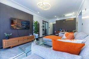 A modern living room with a flat-screen TV, a sofa with orange cushions, a wooden console, and a glass coffee table. - Cozy 2 BR with Heater,Gym,Pool,ample parking on 3floors at Lavington,Nairobi (Nairobi)