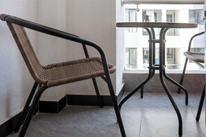 A wicker chair with a metal frame, a small table with a metal frame, and a view of buildings through a window. - Cozy 2 BR with Heater,Gym,Pool,ample parking on 3floors at Lavington,Nairobi (Nairobi)