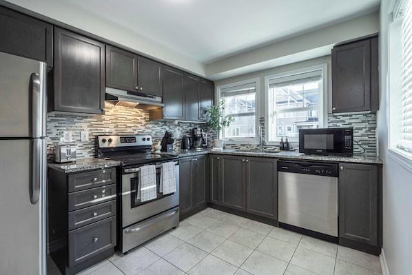 A modern kitchen with dark cabinetry, stainless steel appliances, and a tiled backsplash.