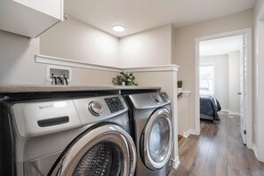 A laundry area with two front-loading Samsung washers, a small potted plant, and a door leading to another room.