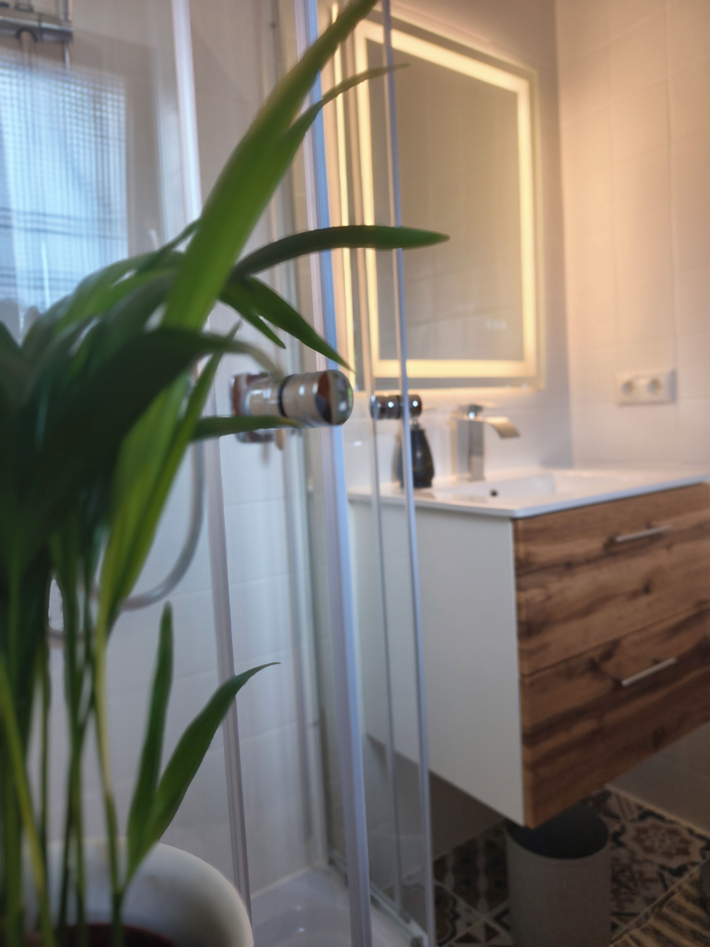 A bathroom with a glass shower enclosure, a wooden vanity, and a mirror above the sink.