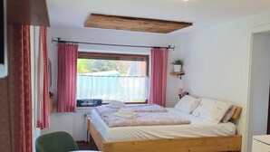 Un dormitorio con cama de madera, una mesa redonda, una silla verde, una ventana con cortinas y una lámpara en el techo.