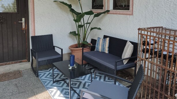 Un espacio al aire libre con un sofá, dos sillones, una mesa y una planta en maceta.